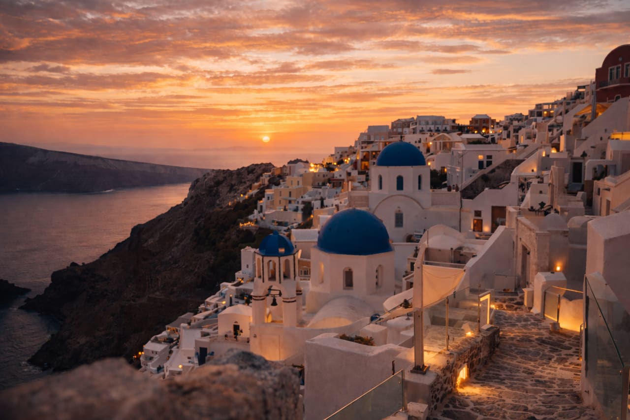 Case bianche e cupole blu di Oia a Santorini sullo sfondo di un tramonto intenso sul Mar Egeo